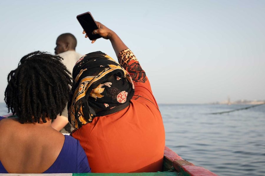 Oumu, vecina de Yaraax, ha intentado cruzar Europa en cayuco y desde su propio barrio y quiere volver a intentarlo. En la imagen, se hace una selfie junto a su hermana, sentadas en un cayuco pesquero de Yaraax. | Sara Aminiyan